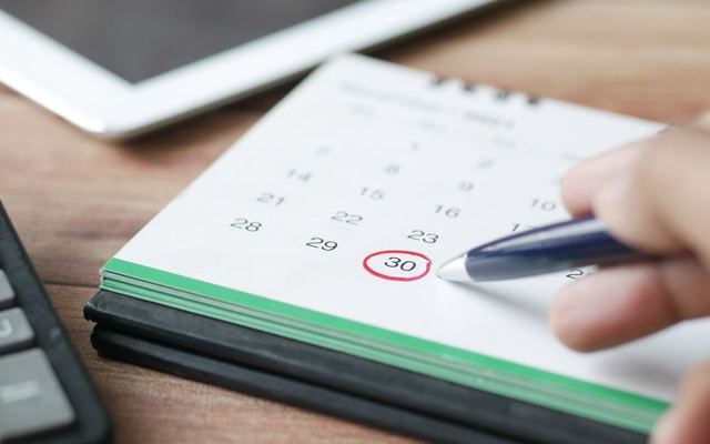 A hand circling a date on a desk calendar